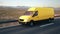 Yellow delivery van driving along a desert road into the sunset