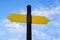 Yellow direction sign on the pole against the blue sky. Yellow arrow signal against sky