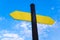 Yellow direction sign on the pole against the blue sky. Yellow arrow signal against sky