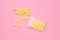 Yellow dragee candies and container on pink background, flat lay