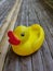 A yellow duck toy with a red beak placed on a wooden plank