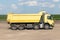 Yellow dump truck with motion effect at the construction site outside the city. Road works on an intercity highway on a cloudy day