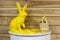 Yellow Easter bunny on white semicircular wooden table with feathers, twigs and a bag with plants