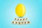 Yellow easter egg on a blue background. Happy Easter, word written on wood blocks. Background