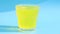 Yellow effervescent tablet with vitamin C in glass on a blue background.
