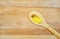 Yellow essential oil in small clear glass bottle in wooden spoon on wooden background. Top view, copy space