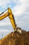 A yellow excavator boom with a bucket digs a pile of earth