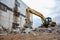 Yellow excavator with bucket at demolition of tall building. Hydraulic machine for demolish. Backhoe destroys concrete