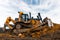 Yellow excavator in career moves overburden. Bulldozer combs the ground, with the bright sun and nice blue sky in the