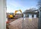 Yellow excavator digger with bucket arm extended working on modern building site with piles of stone and new houses built