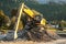 Yellow excavator digger machine digging stones, in river, forest in background