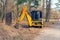 Yellow excavator digs a trench in a city park