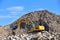 Yellow excavator at landfill for disposal of construction waste. Backhoe dig gravel at mining quarry on blue sky background.