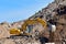 Yellow excavator at landfill for disposal of construction waste. Backhoe dig gravel at mining quarry on blue sky background.