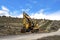 Yellow excavator and orange traffic delineator post beside a mountain road