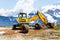 Yellow excavator working near mountains