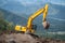 A yellow excavator works in the mountains. Construction of roads