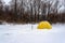 Yellow fishing winter tent stands with an ice-hole in the winter on the ice near the edge of the forest on a snow storm