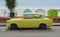 Yellow Ford Anglia motor car on seafront road in front of beach huts.