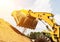 Yellow forklift lifted bucket on a pile with earth, blue sky and sun