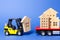 A yellow forklift loads a wooden figure of a house into a truck. Concept of transportation and cargo shipping, moving company