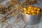 yellow fresh mirabelle plums in a metal pot with sea buckthorn branches and berries on the wooden old blue table