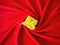 Yellow gift box with yellow ribbon on center spiral red silk background. Aerial.