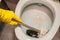 A yellow gloved hand cleans the toilet bowl with a brush