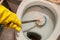A yellow gloved hand cleans the toilet bowl with a brush