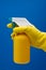 Yellow gloved handing with spray bottle on blue