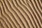 Yellow golden sand on sea beach top view close up, ribbed dry sand surface pattern, wavy curved diagonal lines texture