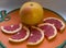 Yellow grapefruit with a red blush on the peel and slices with dark red pulp lie on an orange cutting board.