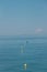 Yellow and green buoys on blue water of Mediterranean Sea lead to sailing catamaran on horizon on sunny day