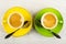 Yellow, green cups with coffee, spoons on saucers on wooden table. Top view