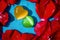 Yellow and green gem stone hearts side by side on blue wet surface surrounded by red rose petals. Love and romance background