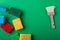 Yellow, green, red, blue sponges with paint brush on green colored paper background, copy space, top view, flat lay