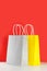 Yellow and grey shopping or gift bags on wooden desk against red background