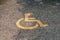 Yellow handicapped symbol of wheelchair painted on asphalt on a parking lot, sign of parking space for disabled visitors. Empty