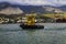 Yellow harbor tug close-up against the backdrop of the seaport and mountains.