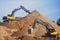 Yellow heavy excavator and bulldozer excavating sand and working during road works, unloading sand and road metal during construct