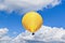 Yellow hot air balloon is suspended in the sky, with wispy white clouds in the background