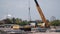 Yellow hydraulic truck crane unloads reinforced concrete piles from a truck at a construction site.