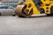 A yellow industrial road roller rushes over the fresh asphalt in light blur