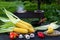 Yellow juicy corn with green leaves lies on a wooden table in the summer garden against the backdrop of a grill