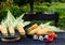 Yellow juicy corn with green leaves lies on a wooden table in the summer garden against the backdrop of a grill