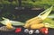 Yellow juicy corn with green leaves lies on a wooden table in the summer garden against the backdrop of a grill