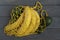 A yellow knitted string bag with bananas and avocado lies on a gray wooden background. The concept of zero waste