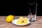 Yellow lemons with lemon pieces on a ceramic plate and a glass behind