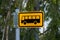 Yellow local bus stop sign in Finland, with green trees in the background