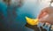 Yellow lonely floating paper boat in hand. Colorful sailing ship in big blue spring puddle, river water.Warm wet rainy